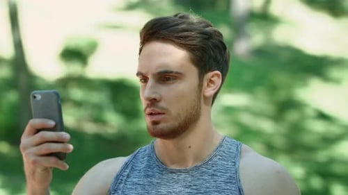 Sport Man Looking Mobile Phone and Running in Park. Man Athlete Using Smartphone