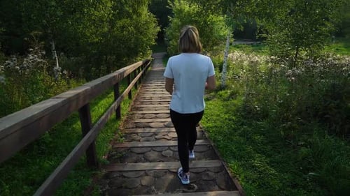 Junges, attraktives, feines Mädchen oder eine Frau in weißem T-Shirt und schwarzer Sporthose, die die Treppe hinuntergeht in