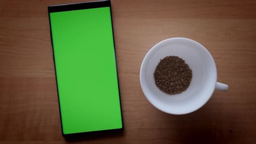 Man Hand Prepares Instant Coffee in White Cup and Phone with Green Screen on Table