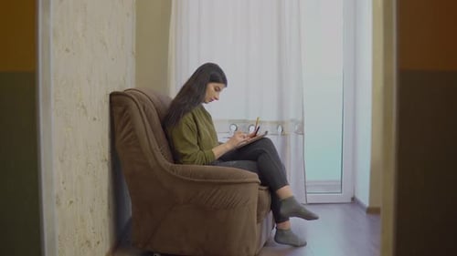 Woman Writing in Notebook in Cozy Armchair