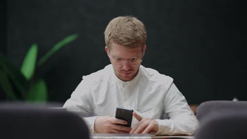 Junger Mann mit Brille mit Handy in den Händen schaut auf Bildschirm und SMS Männlicher Benutzer