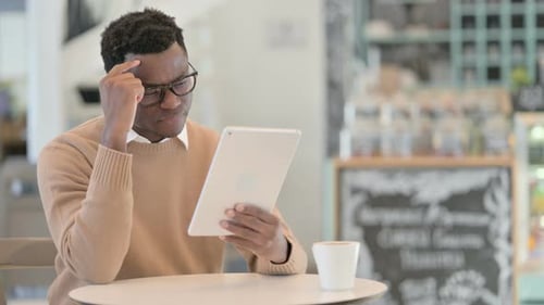 Creative African Man Reacting to Loss on Tablet in Cafe
