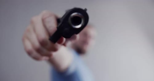Der Mann droht mit einer Pistole, richtet die Pistole auf die Kamera. Nahaufnahme des Laufs einer Pistole.