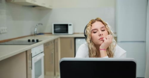 Sleepy Young Woman with Curly Hair Listens To Online Lecture