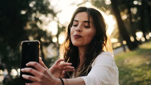 Young pretty woman taking selfie with smartphone in a green park