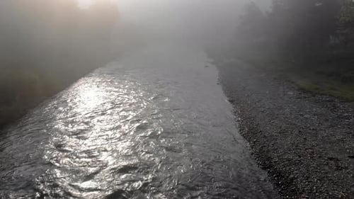 River Flowing Through Mountain Village in a Foggy Morning