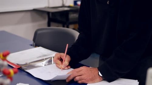 A college biology professor grading homework assignments from his students and taking notes in his c