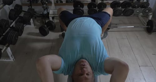 Grown man in a gym lying on bench and raises damn over head