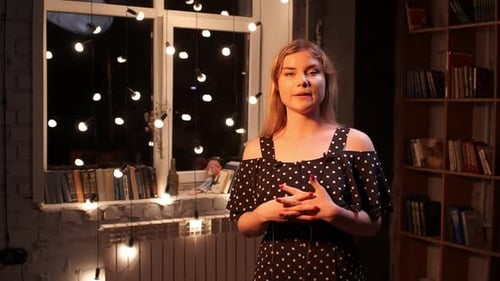 Junge Bloggerin schaut in die Kamera und redet über etwas, das in einem dekorierten Raum steht