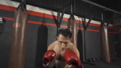 Strong caucasian man punching in front of camera, combat punches in boxing sport club workout