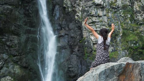Woman Sits near Waterfall in Nature