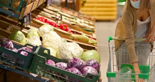 Woman Buys Groceries in a Supermarket Chooses Vegetables and Puts and a Cart