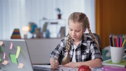 Mädchen macht Hausaufgaben im Zimmer, während sie während der Quarantäne mit Laptop am Tisch sitzt