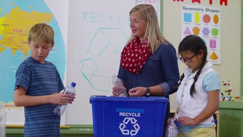 Teacher and students in school classroom putting bottles in recycle bin