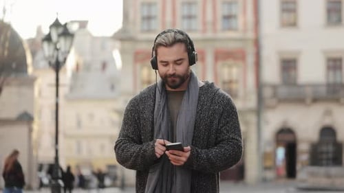 Man Smiling Using Smartphone and Headphones in City Square