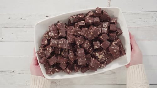 Flat lay. Step by step. Macadamia fudge cut in small cubes on a white serving dish.