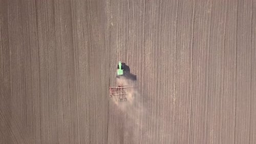Top Down Aerial View of Green Tractor Cultivating Ground and Seeding a Dry Field