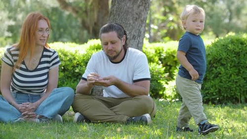 Family Spends Time in the Park Parents Sitting on the Grass on Their Son Gives Them Plucked Grass