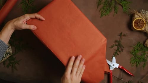 Hands Wrapping Rustic Holiday Gift on Brown Tabletop
