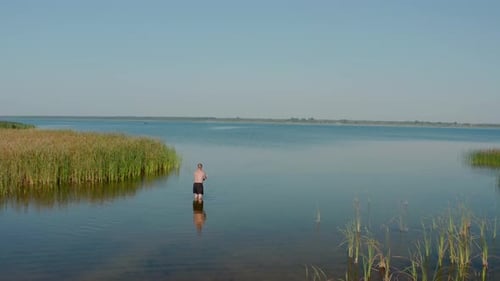 Drohnen-Luftaufnahme. Ein Mann steht im See und fischt am Sommermorgen