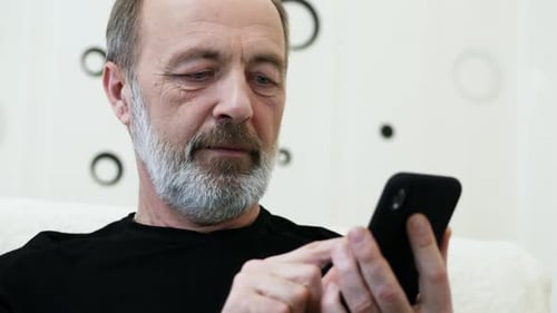 Middle-aged Man with a Gray Beard Uses the Phone at Home, Close-up