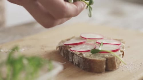 Hand Sprinkling Fresh Sprouts on Radish Sandwich