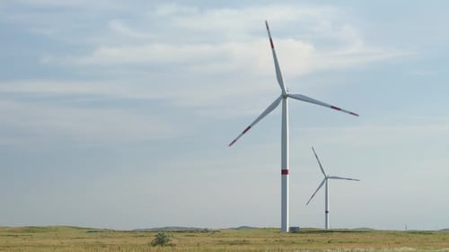 Bewegen Sie die Blätter einer großen Windkraftanlage in einem Feld vor dem Hintergrund des orangefarbenen Sonnenuntergangs auf dem