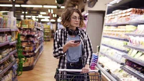 Woman Shopping in Grocery Store Aisle Looking at Phone