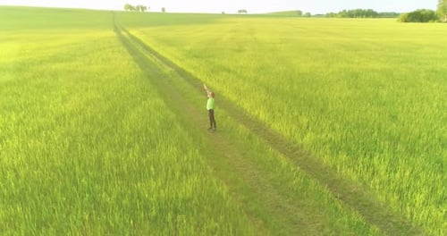 Sporty Child Standing in Green Wheat Field with Raised Hands Up