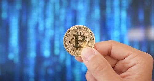 Hand Holding a Bitcoin in Front of Tech Background