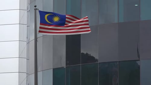 Waving Malaysian Flag in Front of Modern Corporate Building