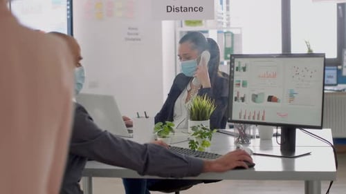 Collègues portant des masques faciaux assis au bureau dans le nouveau bureau normal de l'entreprise