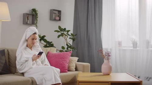 Woman in Robe Using Smartphone on Couch