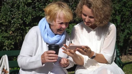 Woman and Senior Woman Sharing Smartphone Outdoors