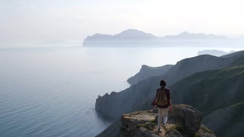 Young Woman Raises Her Hands Up Standing on the Top of a Mountain