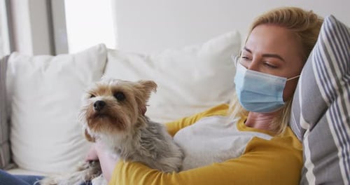 Woman wearing face mask holding her pet dog at home