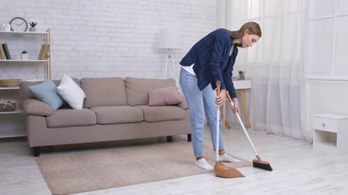 Woman Sweeping Floor with Broom in Living Room