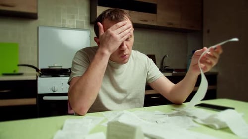 Man Looks Concerned Over Receipts At Kitchen Table