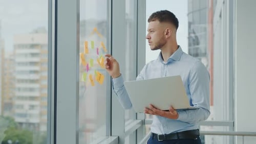 Young Successful Businessman in the Office By the Window Working with a Laptop. The Man Solves