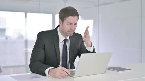 Middle Aged Businessman Thinking and Working on Laptop