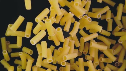 Uncooked Macaroni Pasta Falling on Black Background