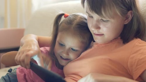Sisters Using Tablet Device Together on Couch
