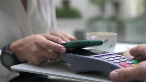 A customer pays for coffee using NFC contactless payment technology on a smartphone in a cafe.