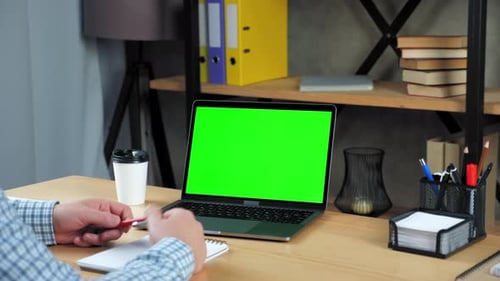 Businessman at office sitting on chair at table tells with green screen laptop