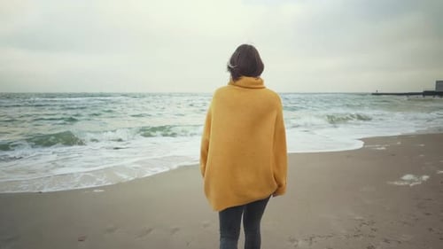 Young Beautiful Woman in Orange Sweater Walking on the Beach in Cold Weather