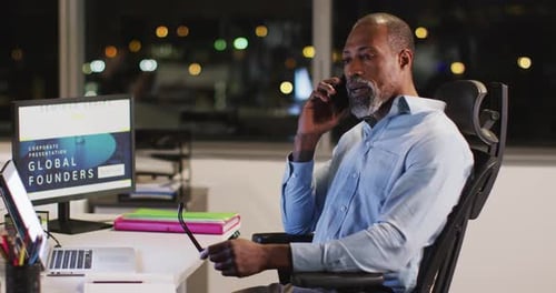 Professional businessman talking on his phone while sitting on his desk in modern office in slow mot