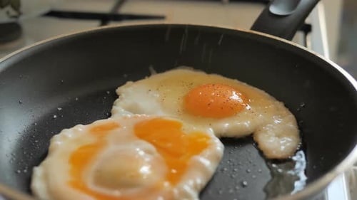 Fried Eggs Cooking in Pan with Salt and Pepper