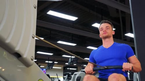 A Young Fit Man Trains on a Rowing Machine in a Gym - Closeup