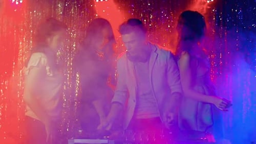 DJ Mixing Music with Dancers in Nightclub Setting