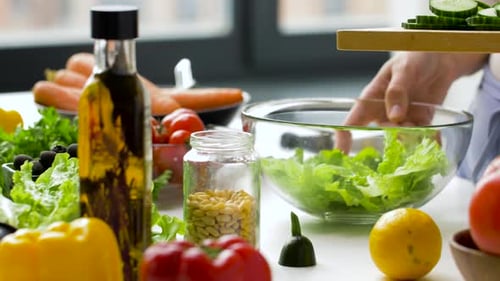 Woman Adding Chopped Cucumber To Vegetable Salad